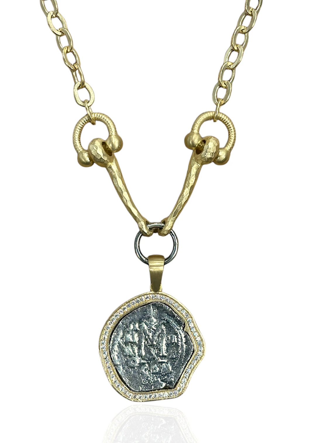 A gold horsebit chain necklace with a silver coin pendant encase by CZs on a white background