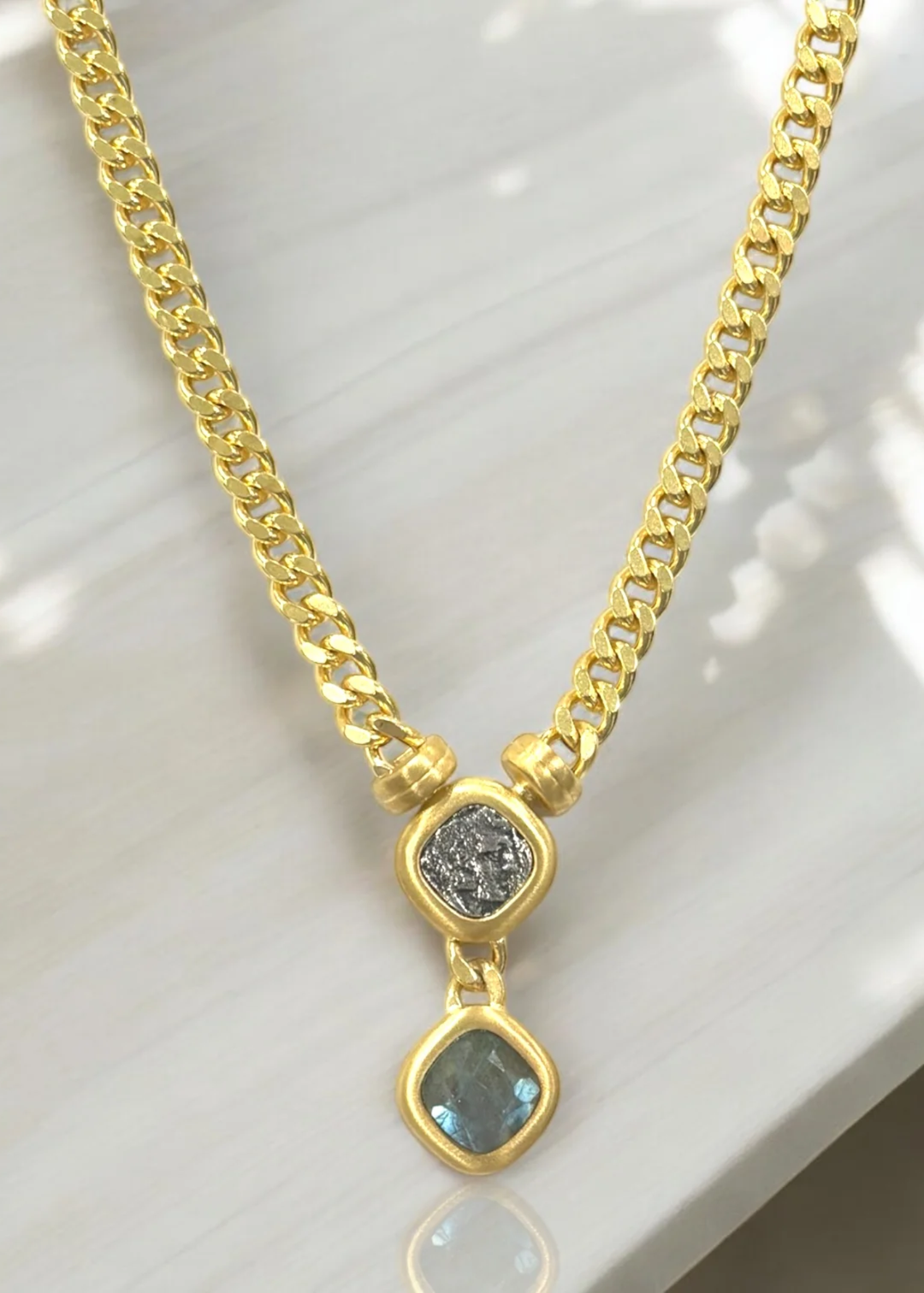Gold chain necklace with a coin and labradorite pendant on a white background