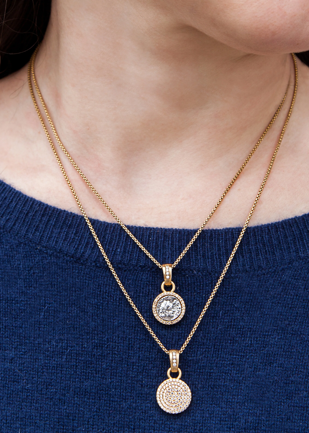 Woman wearing layered necklaces with one being a gold chain necklace with a silver coin pendant framed in gold and CZ pave
