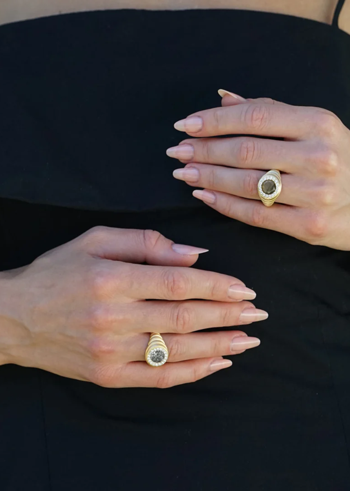 Close up of a woman wearing a gold scalloped ring with a silver coin framed in CZ's