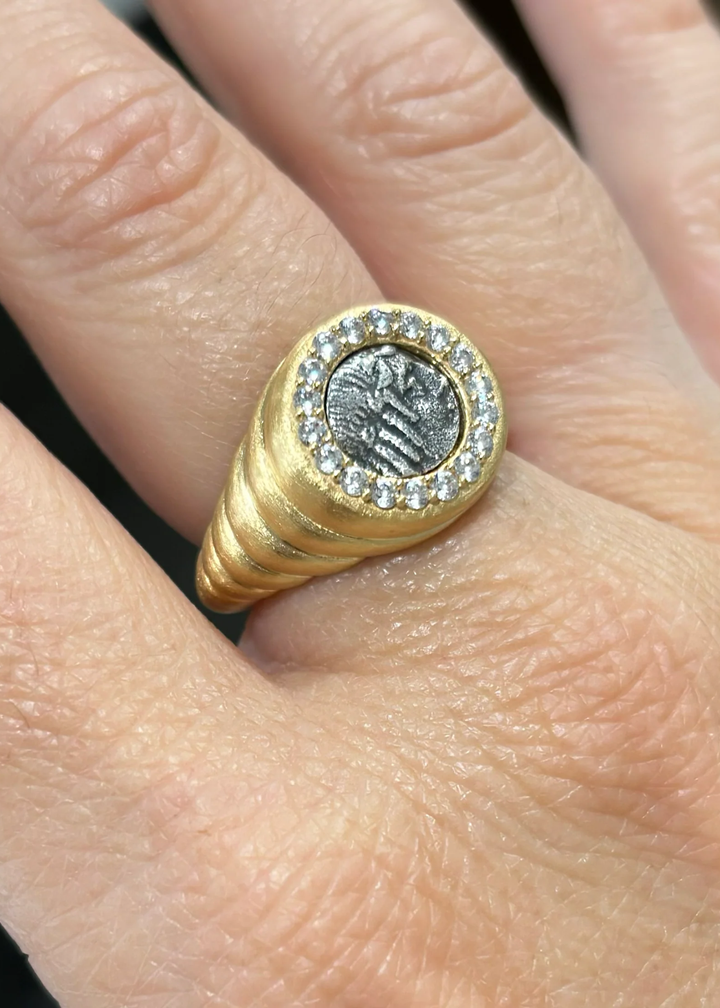 Close up of a gold scalloped ring with a silver coin framed in CZ's on a hand