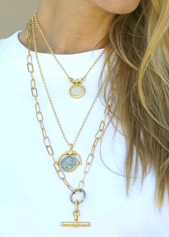 Woman wearing necklaces including a gold necklace with a spinner and vintage coin pendant