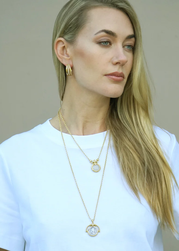 Woman wearing a gold necklace with a spinner and vintage coin pendant