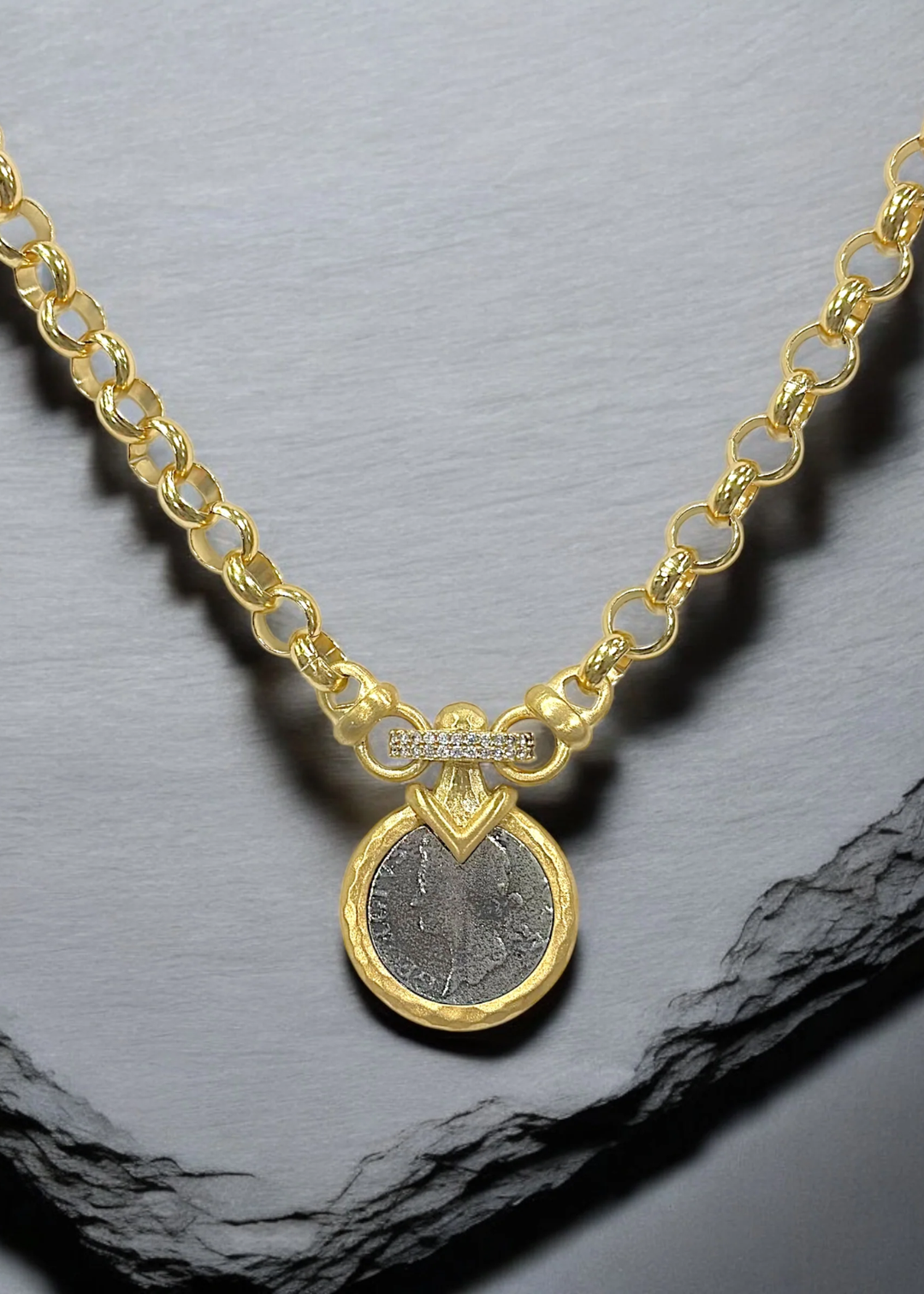Gold chain necklace with a silver coin pendant on a grey background