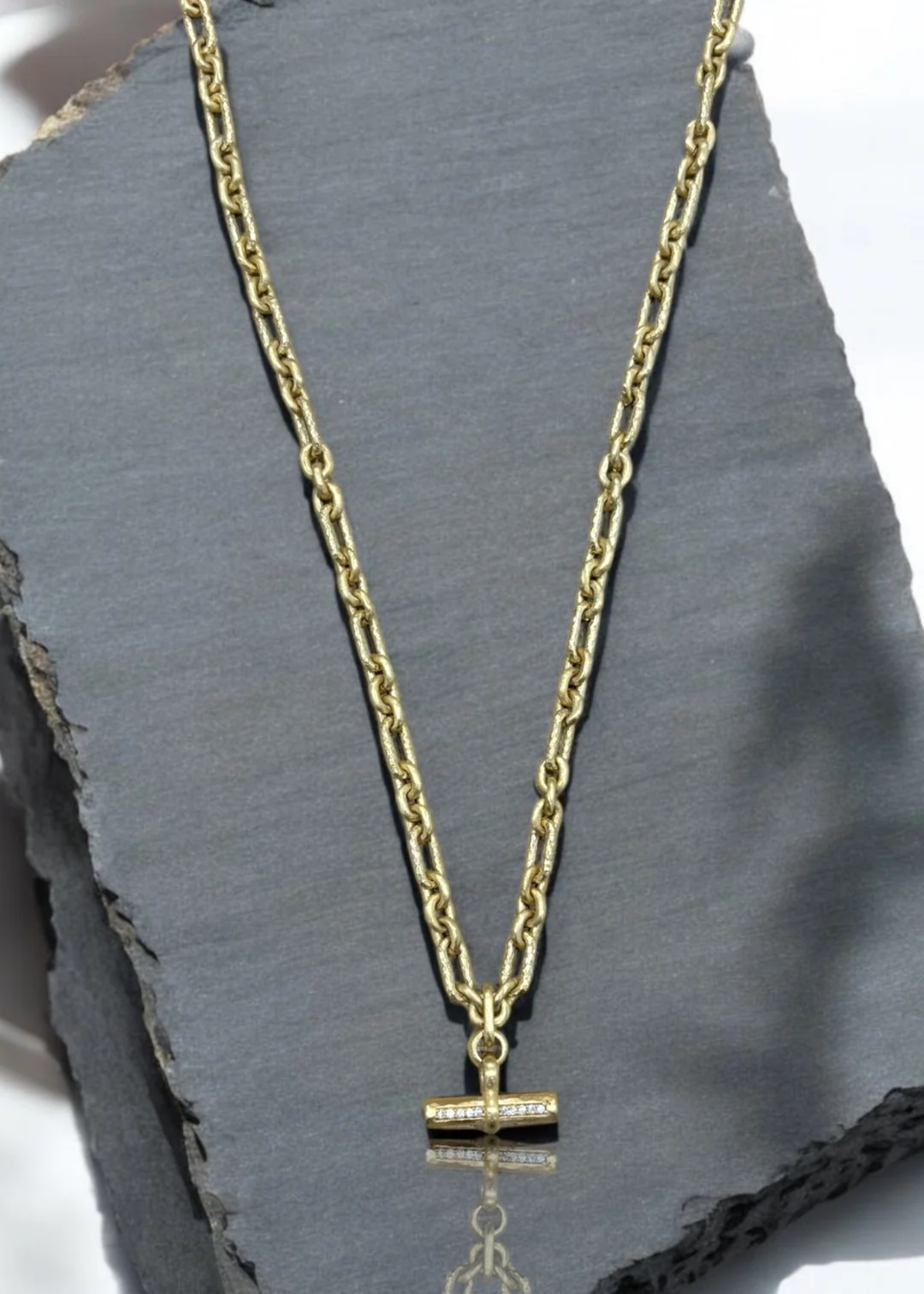 Gold chain necklace with a CZ studded toggle on a grey background