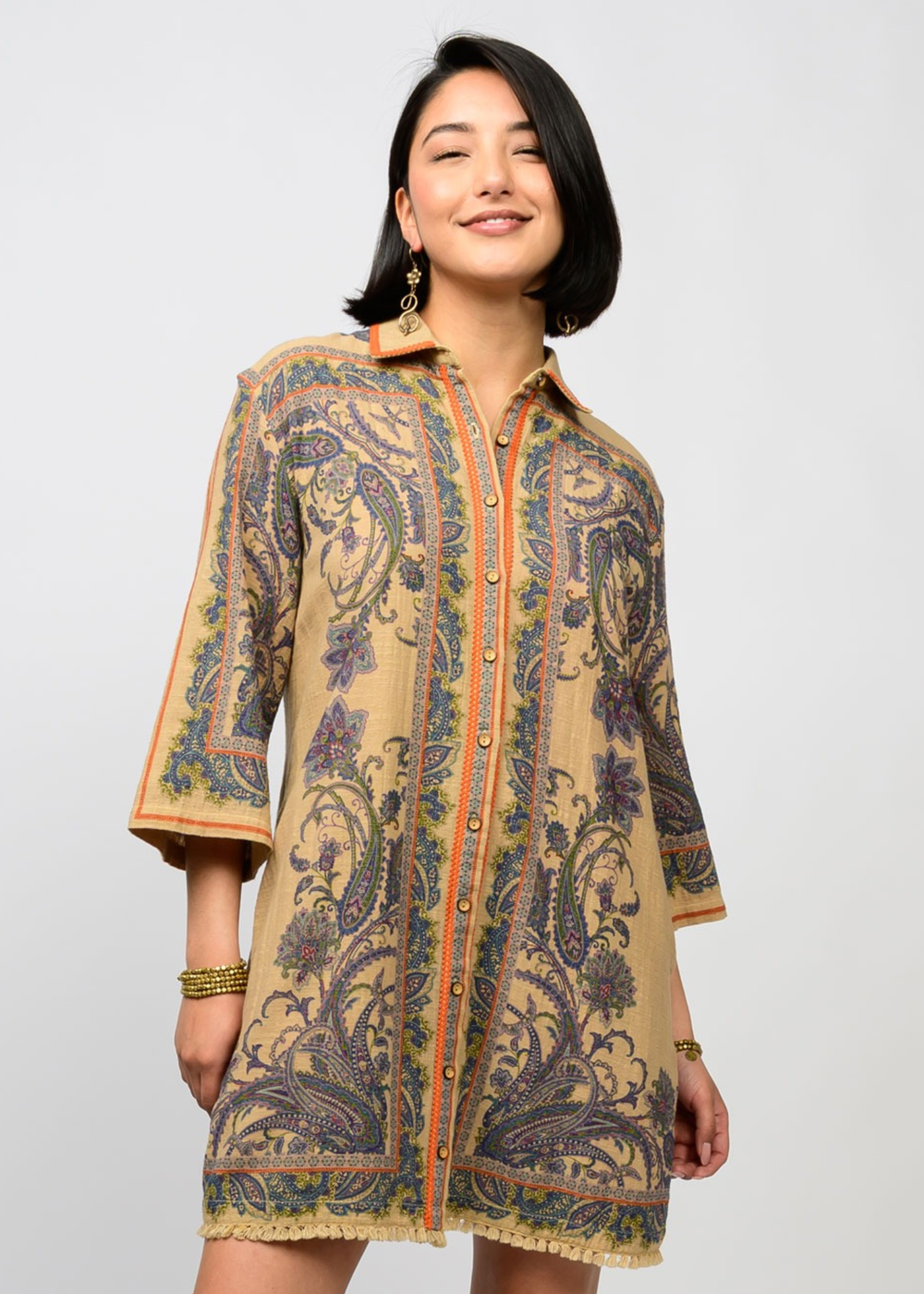 Woman wearing a camel and floral button down dress with 3/4 length sleeves standing in front of a white background