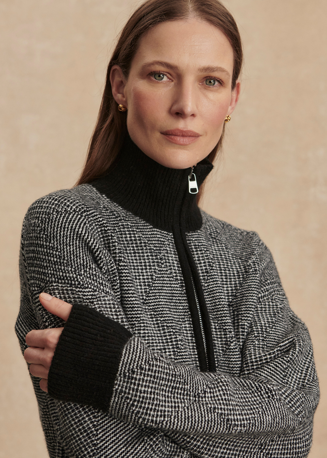 Woman with arms crossed wearing a black knit top with black pants against a tan background