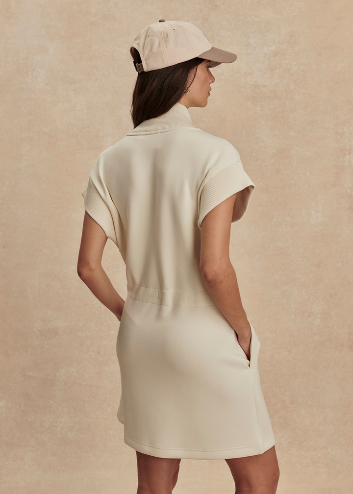 Woman turned around wearing an ivory half zip mini dress