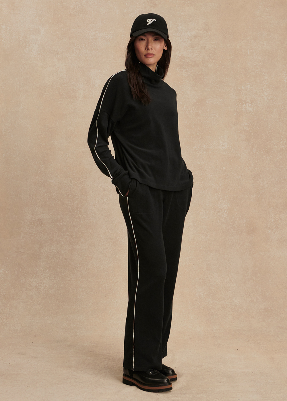 Woman turned to the side wearing a black top and black pants against a tan background