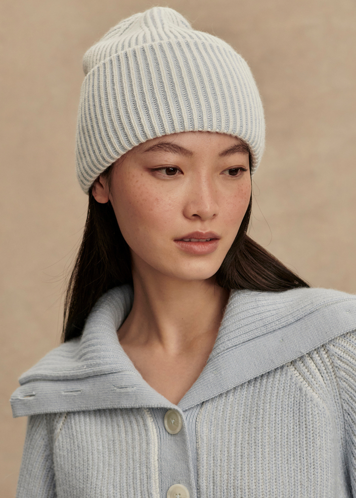 Woman wearing a light blue beanie and a light blue sweater in front of a tan background