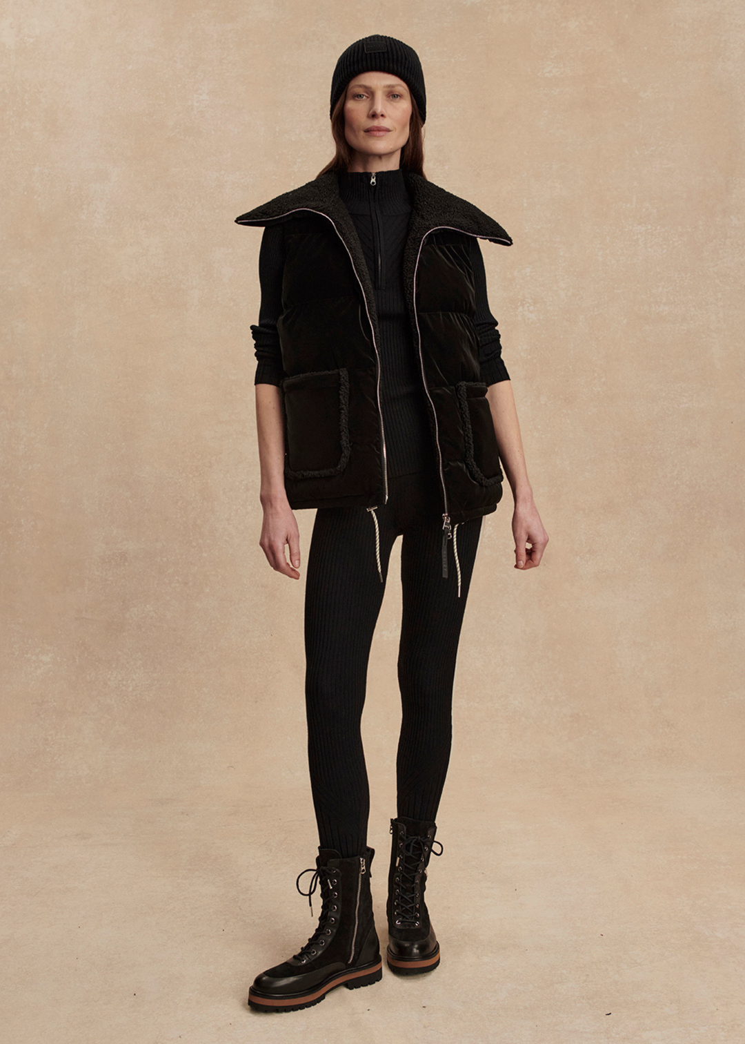 Woman wearing a black outfit with a black puffer vest against a tan background