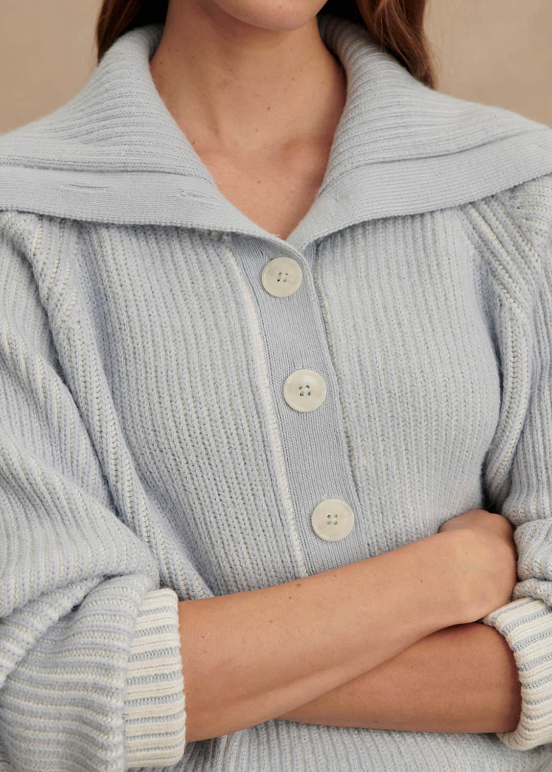 Close up of a woman wearing a light blue ribbed sweater with arms crossed