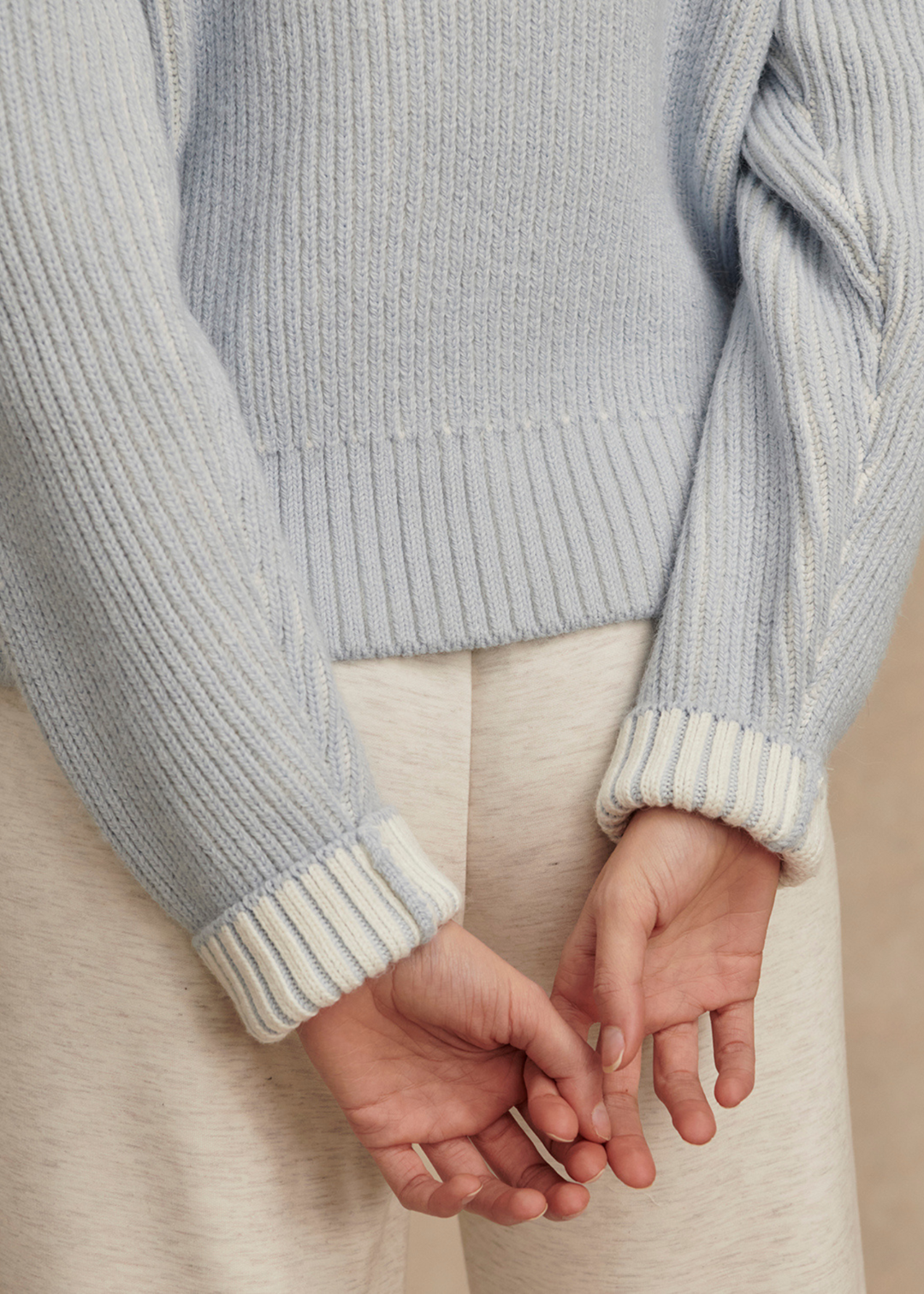 Close of light blue ribbed sweater and folded over white sleeves with hands interlaced