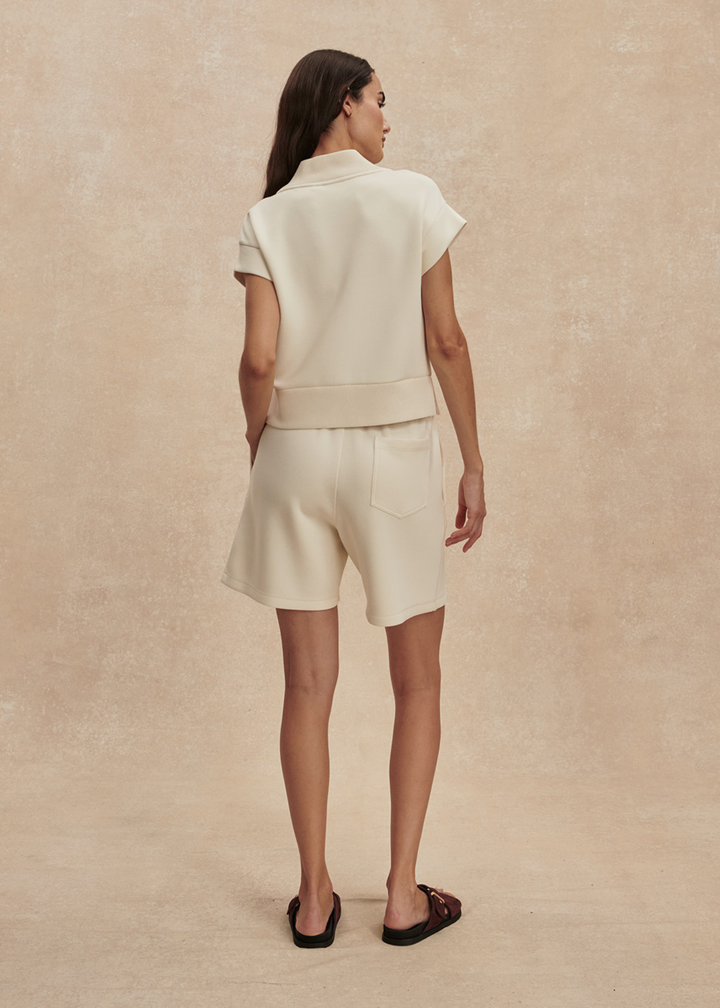 Woman turned around wearing a cream v-neck top with matching shorts