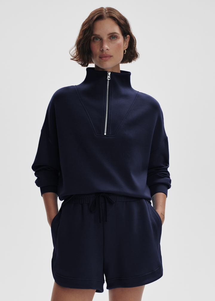 Woman wearing a navy half zip sweatshirt top with matching shorts in front of a white background