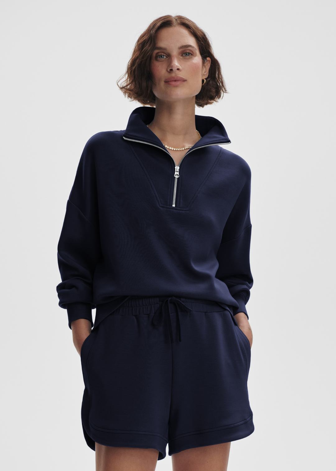 Woman wearing a navy half zip sweatshirt top with matching shorts in front of a white background