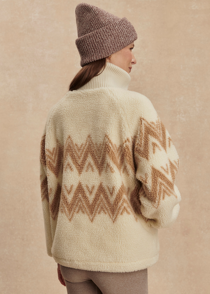 Woman turned around wearing a cream and brown half zip sherpa with a brown beanie and leggings