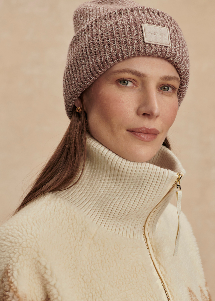 Close up of a woman wearing a cream and brown half zip sherpa with a brown beanie 