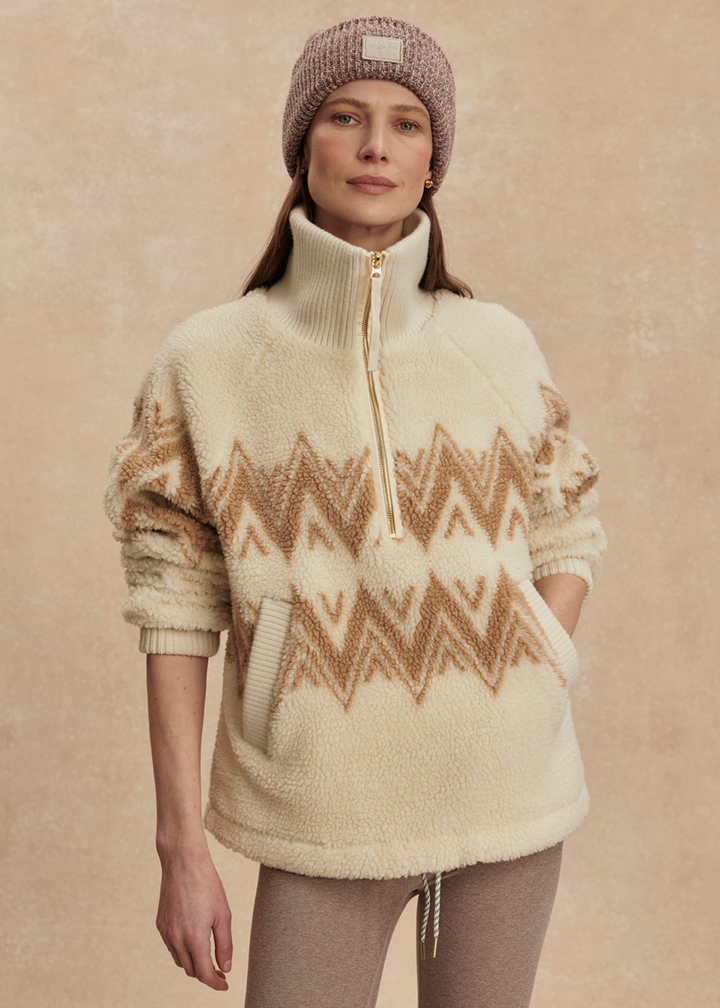 Woman wearing a cream and brown half zip sherpa with a brown beanie and leggings with hand in pocket