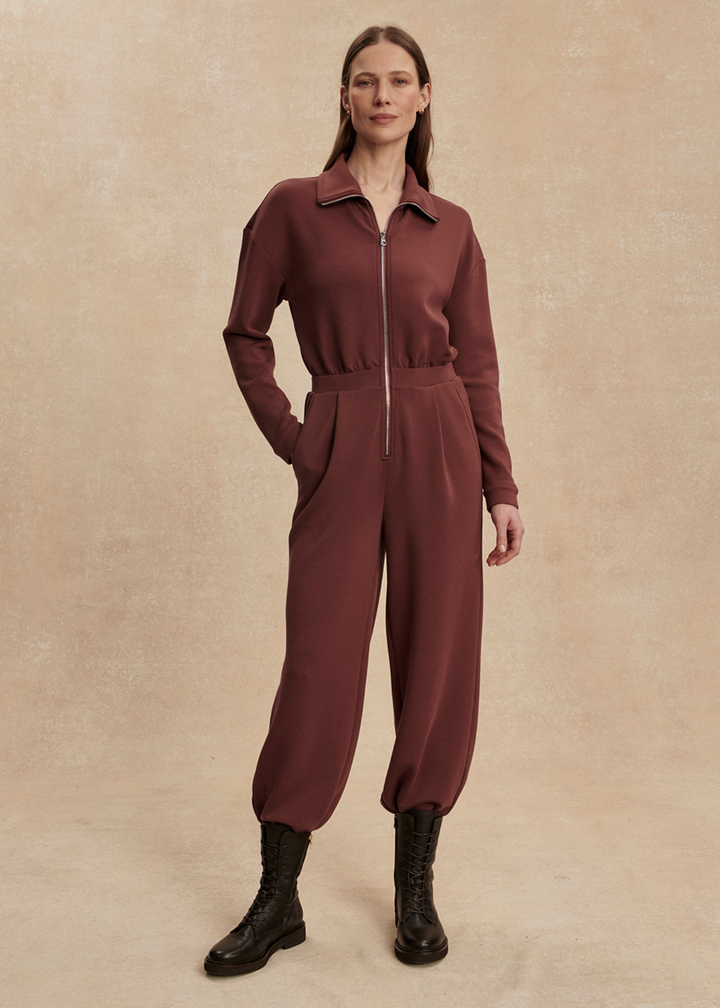 Woman wearing a brown jumpsuit with black boots in front of a tan background