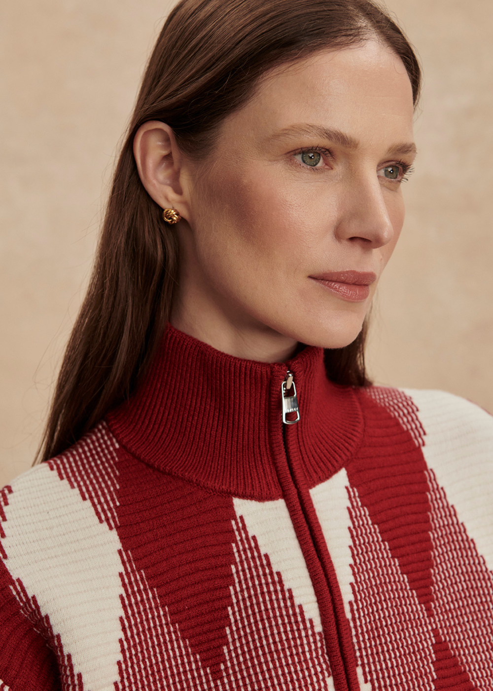 Close up of a woman wearing a red and white patterned sweater against a tan background