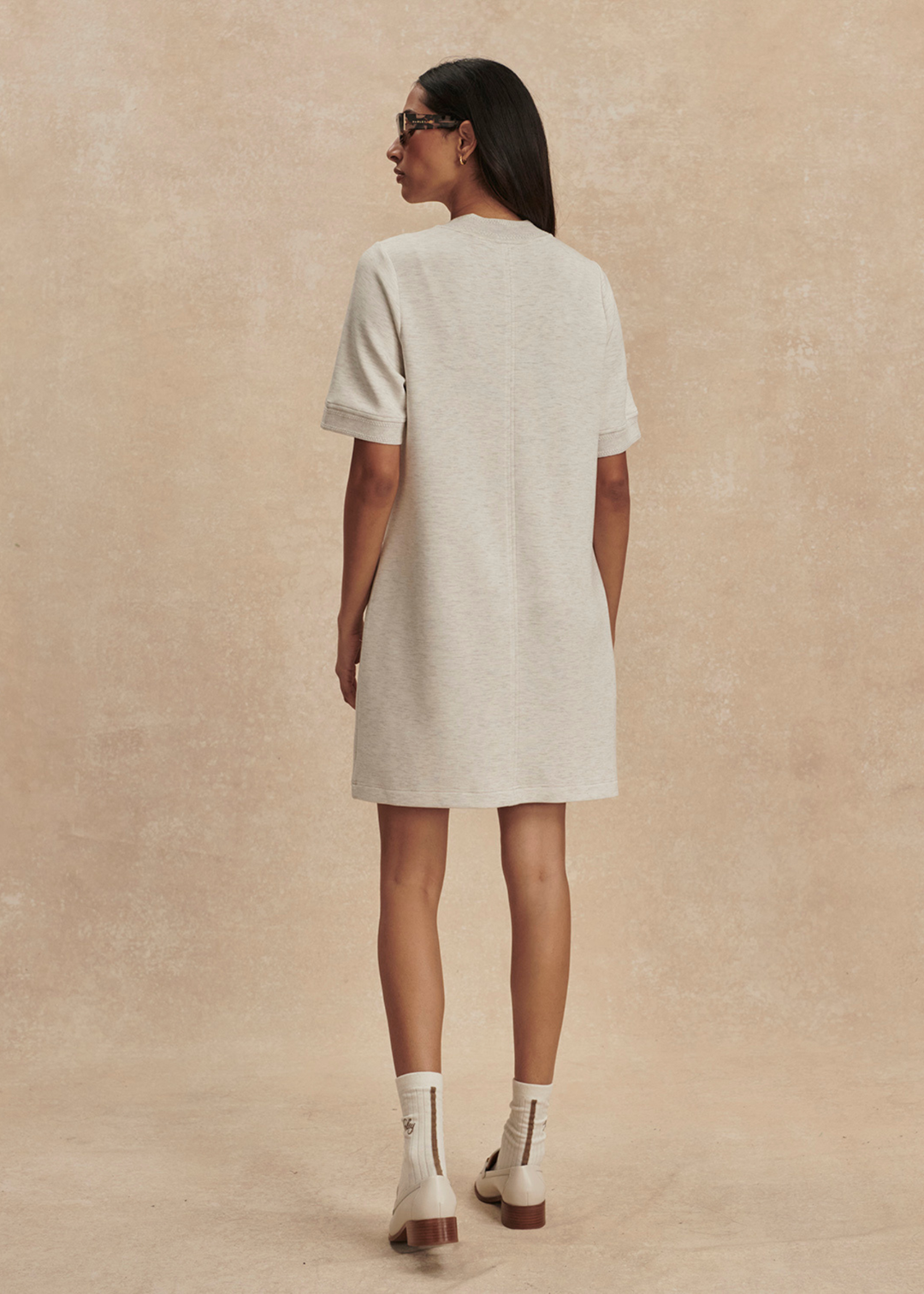 Woman turned around wearing an ivory half zip mini dress