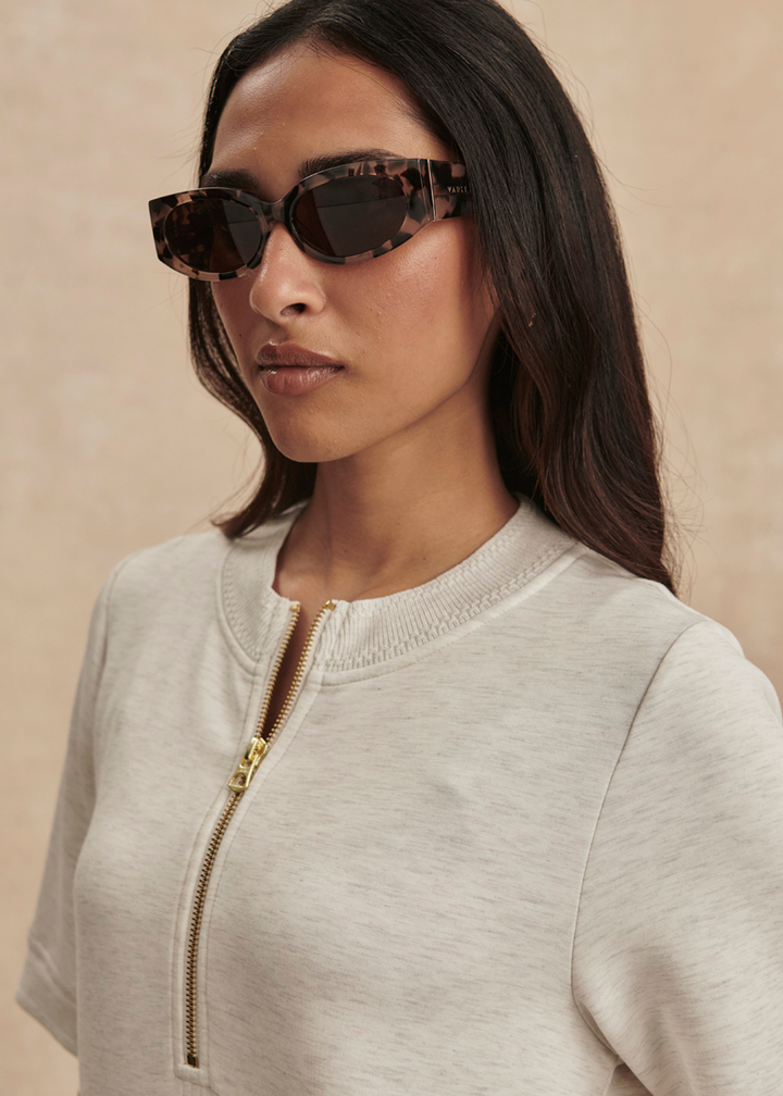 Close up of a woman wearing an ivory half zip mini dress with sunglasses