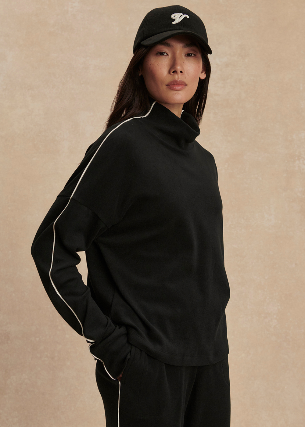 Woman wearing a black set with white trim against a tan background