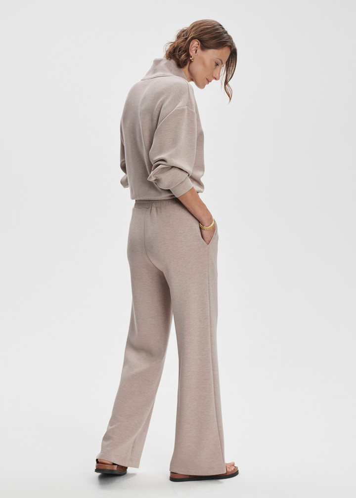 Woman turned to the side wearing taupe wide leg pants with a taupe half zip top against a white background