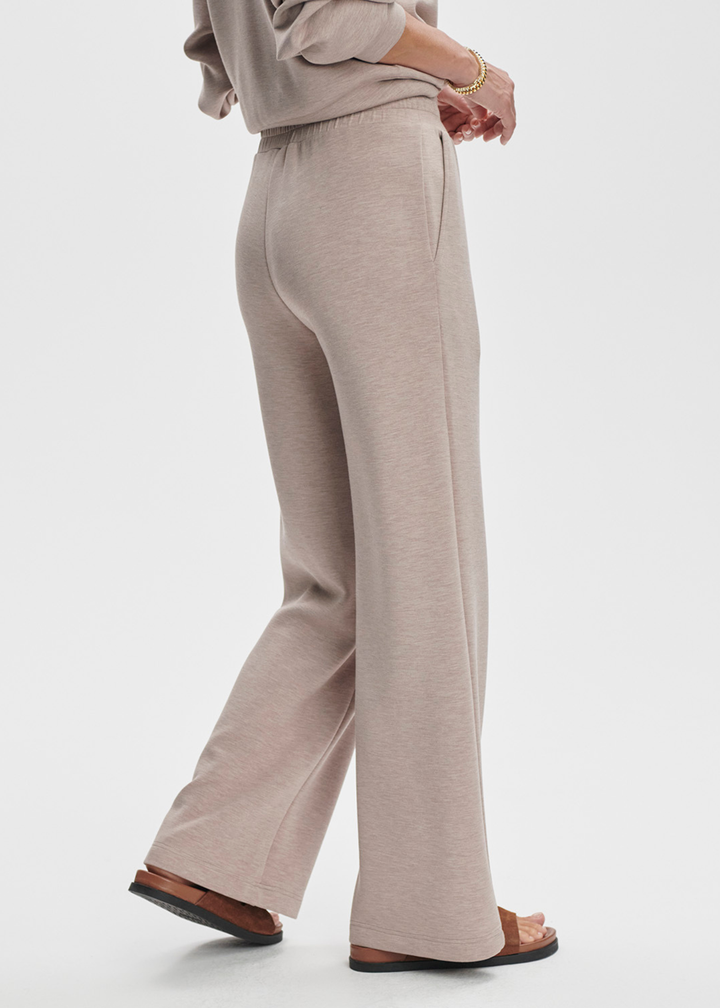 Woman turned to the side wearing taupe wide leg pants against a white background