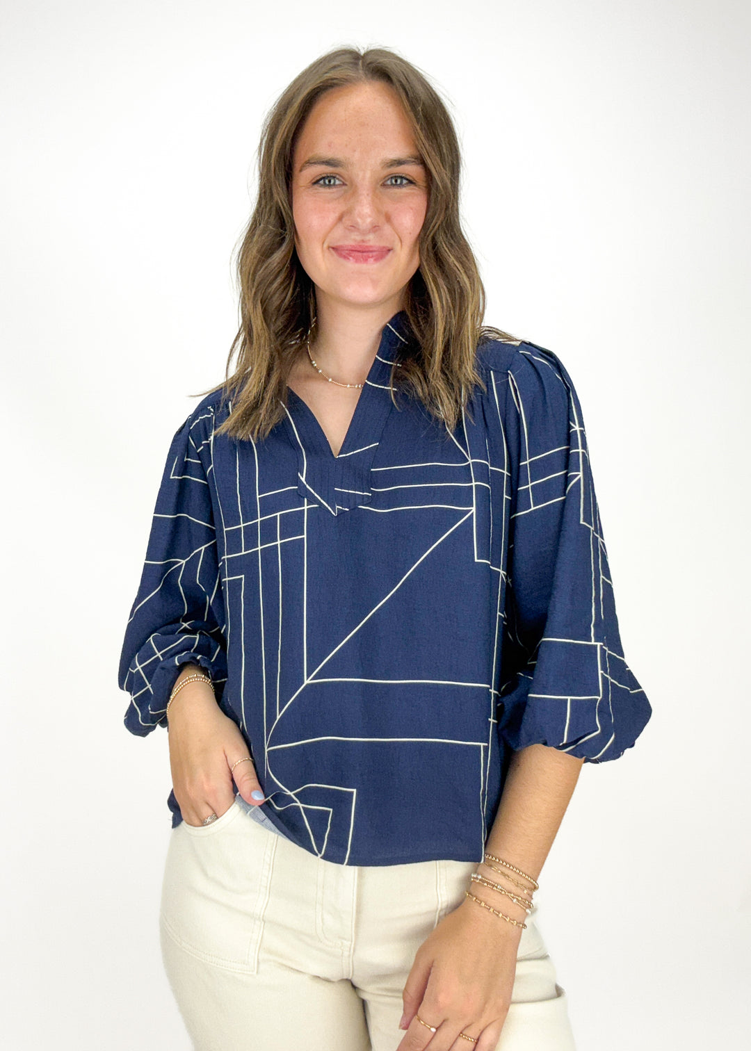 woman wearing navy and white geometric line print top with 3/4 puff sleeves and split neckline
