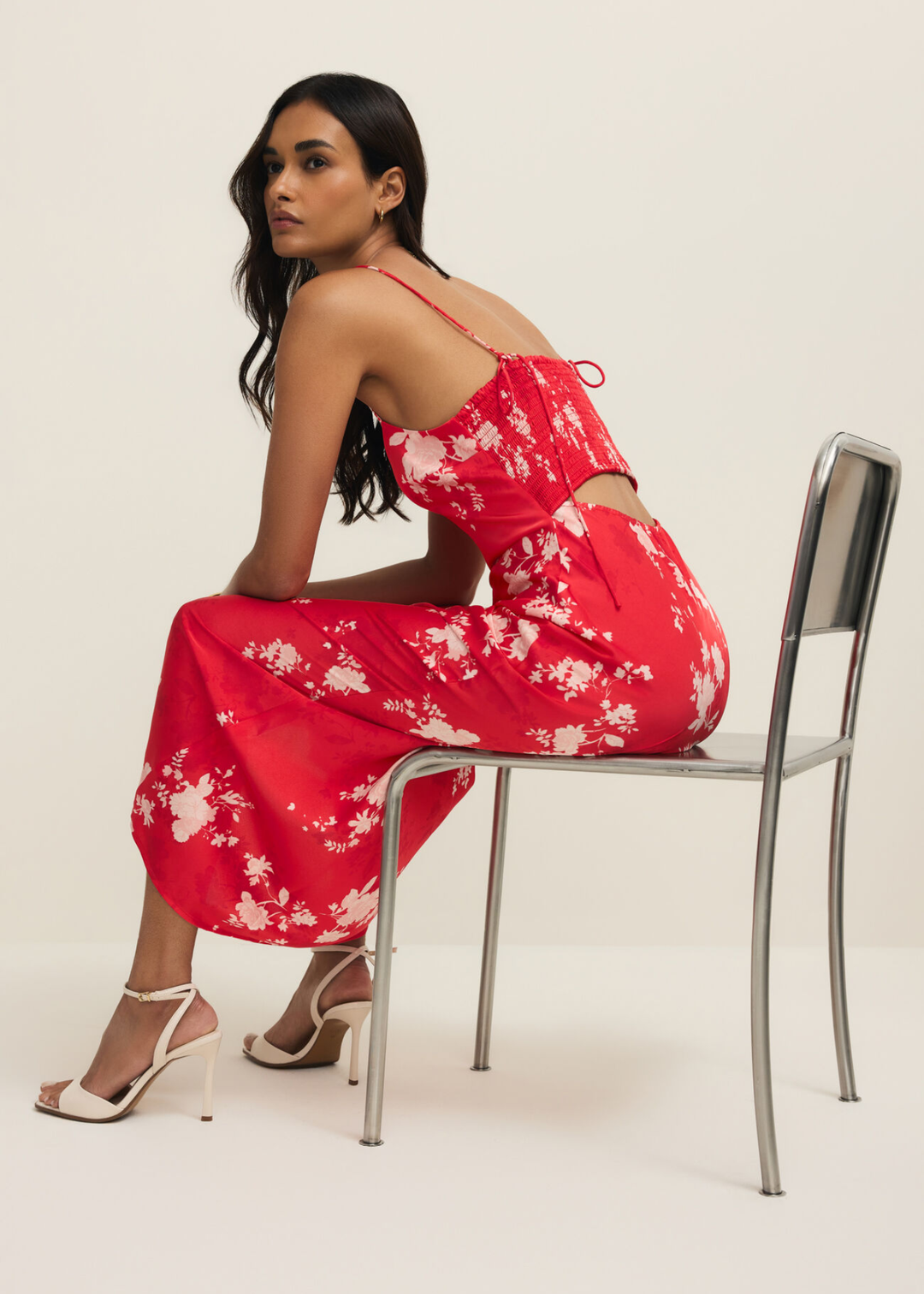 Woman sitting wearing a red and white floral maxi dress against a white background