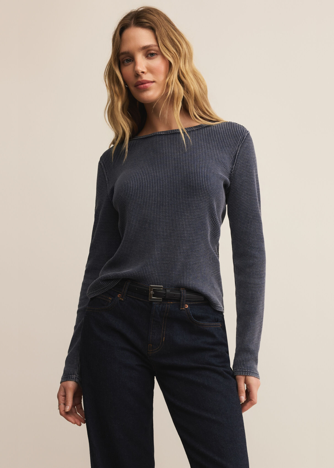 Woman wearing a dark blue long sleeve tee with dark wash jeans against a white background