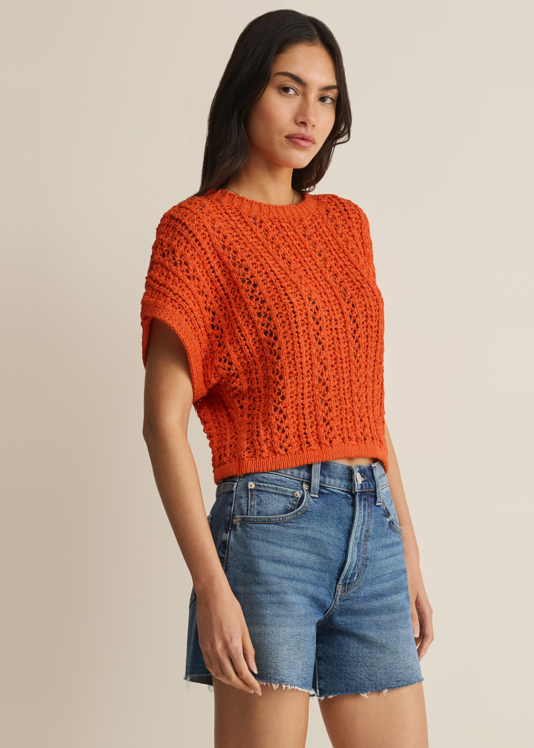 Woman wearing an orange crochet top with denim shorts