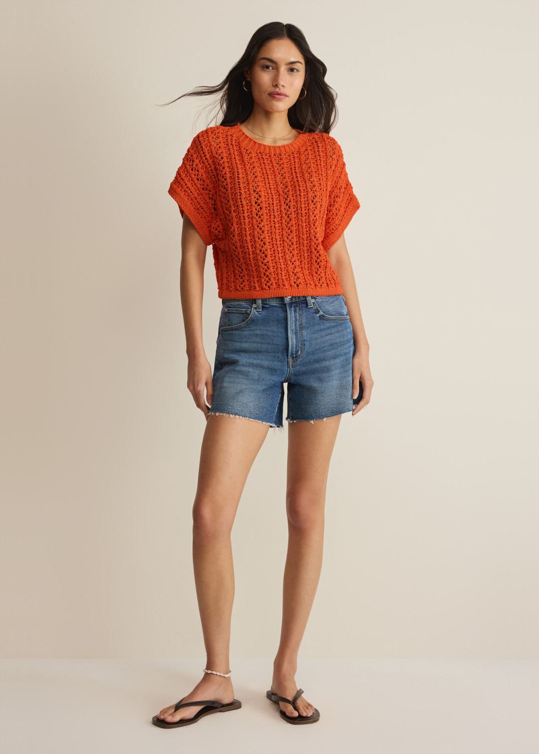 Woman wearing an orange crochet top with denim shorts