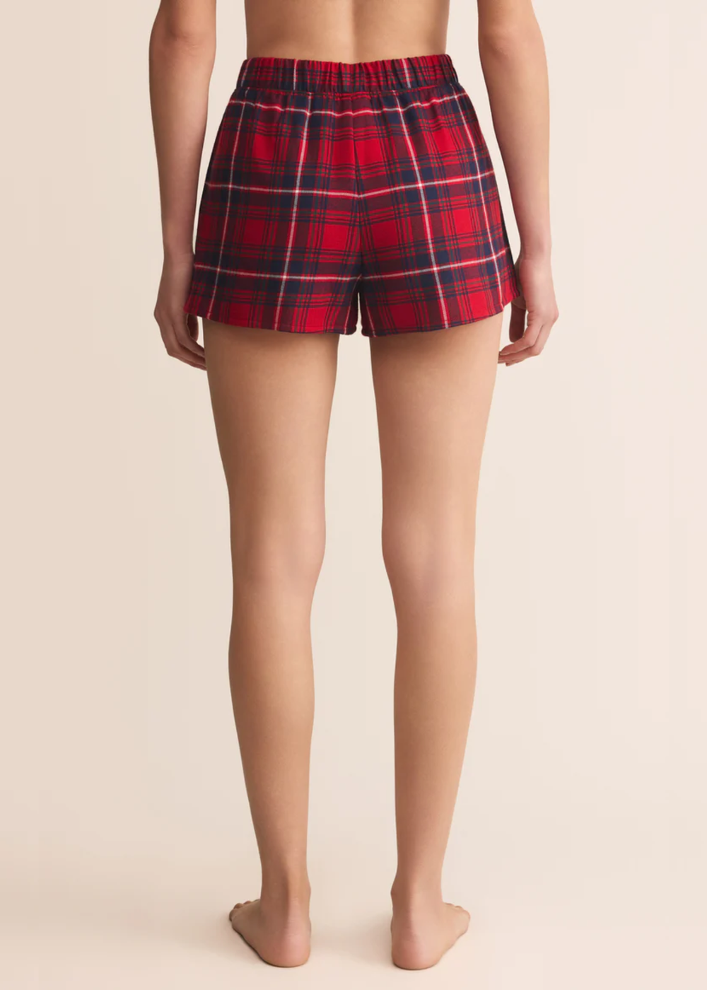 Woman turned around wearing red Christmas plaid shorts in front of a grey background