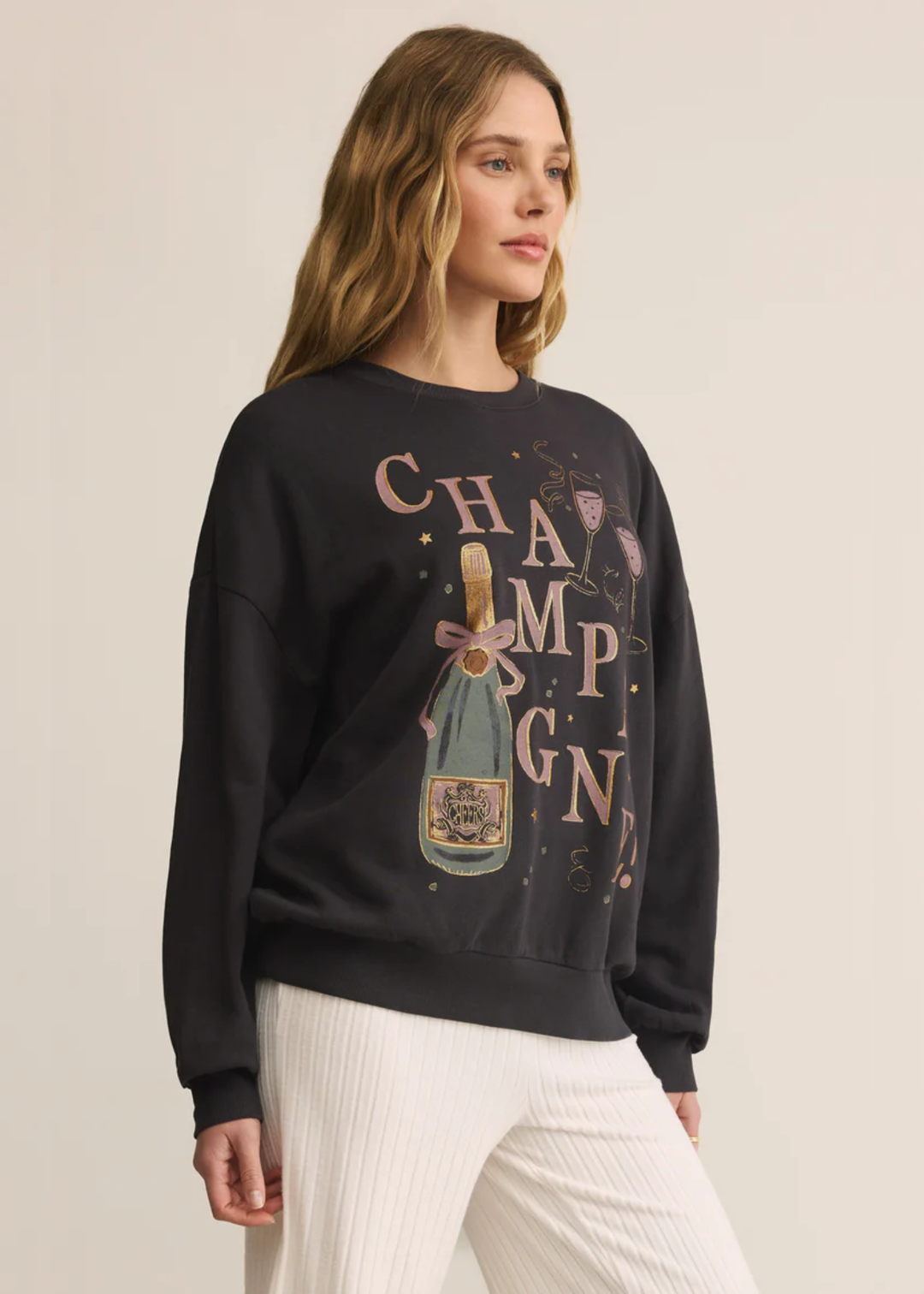 Woman wearing a grey sweatshirt with a champagne graphic and white pants