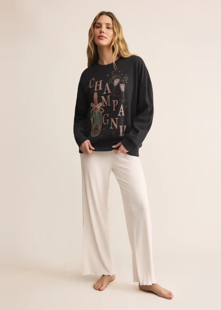 Woman wearing a grey sweatshirt with a champagne graphic and white pants