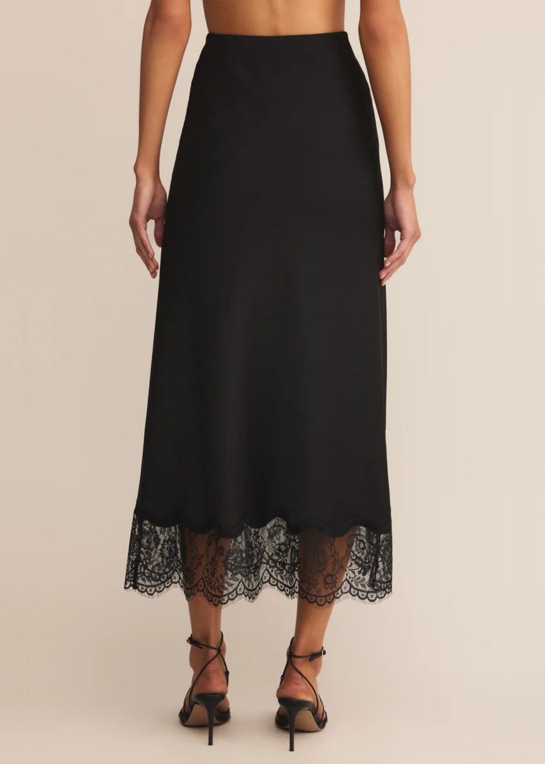 Woman wearing a black satin skirt with a lace trim and black heels