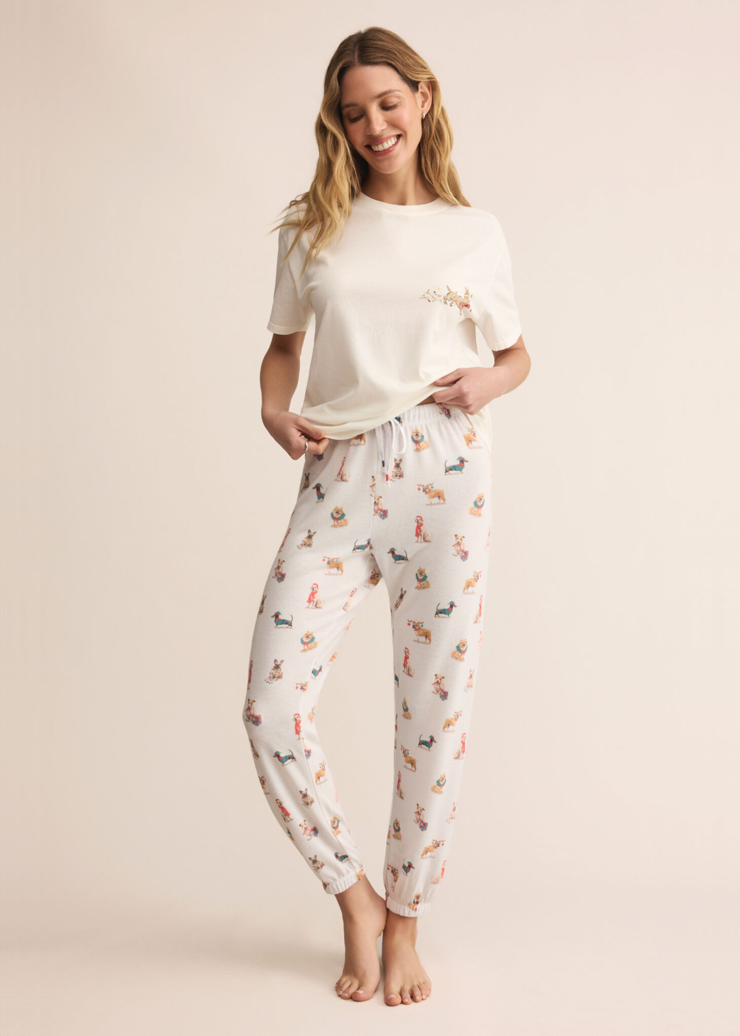 Woman wearing white joggers with a dog graphic pattern in front of a tan background