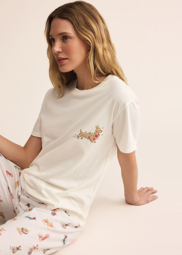 Woman sitting wearing white joggers with a dog graphic pattern in front of a tan background