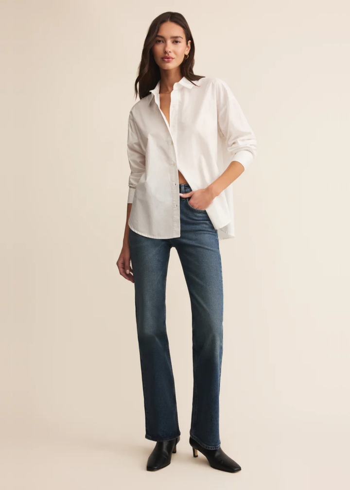 Woman wearing a white button down shirt with jeans and hand in pocket