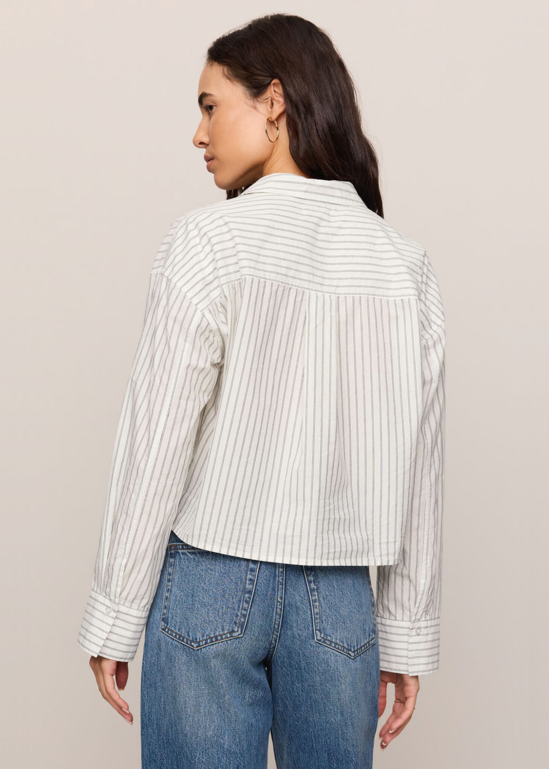 Woman turned around wearing a white striped button down top with jeans