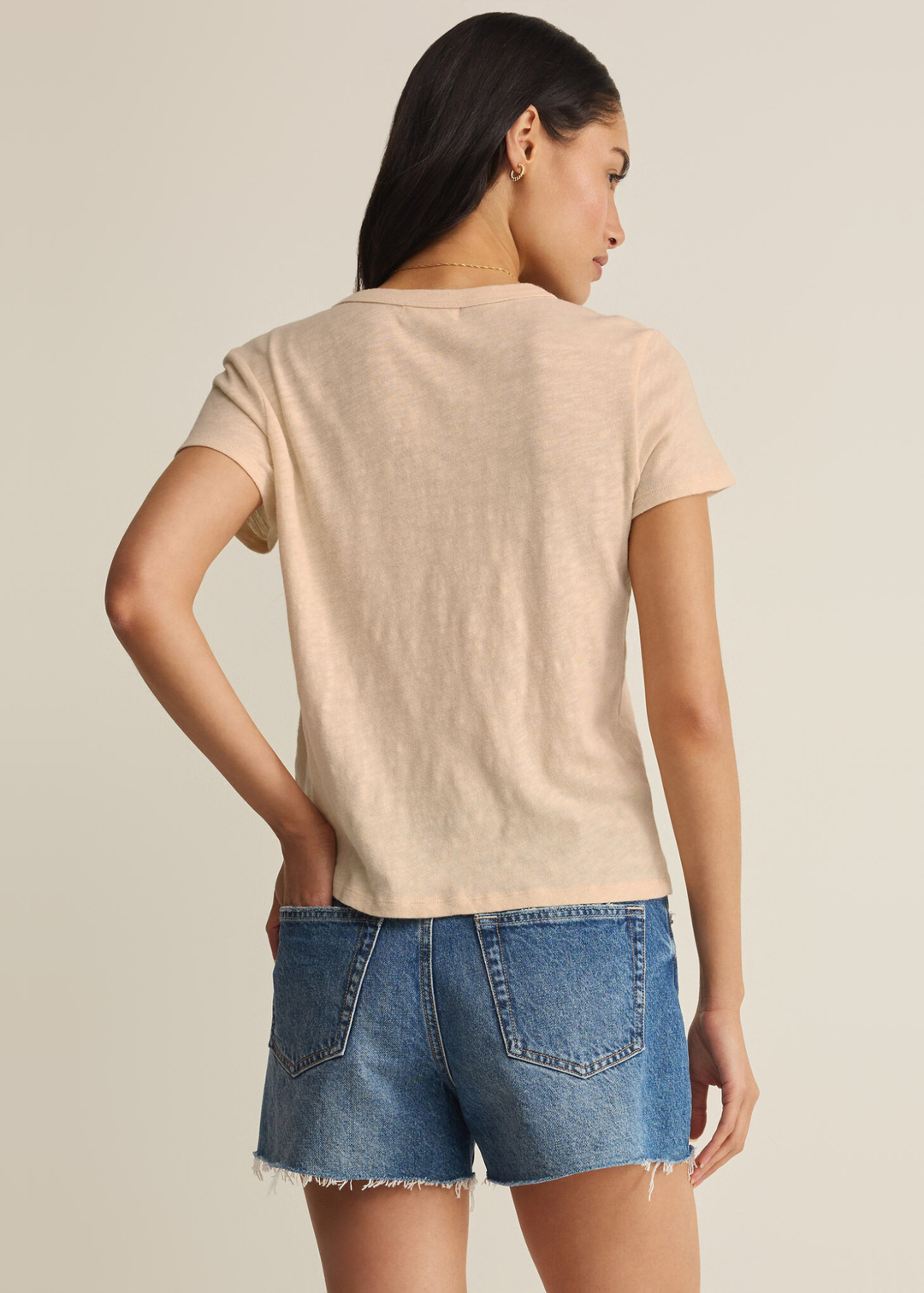 Woman turned around wearing a tan t-shirt with denim shorts