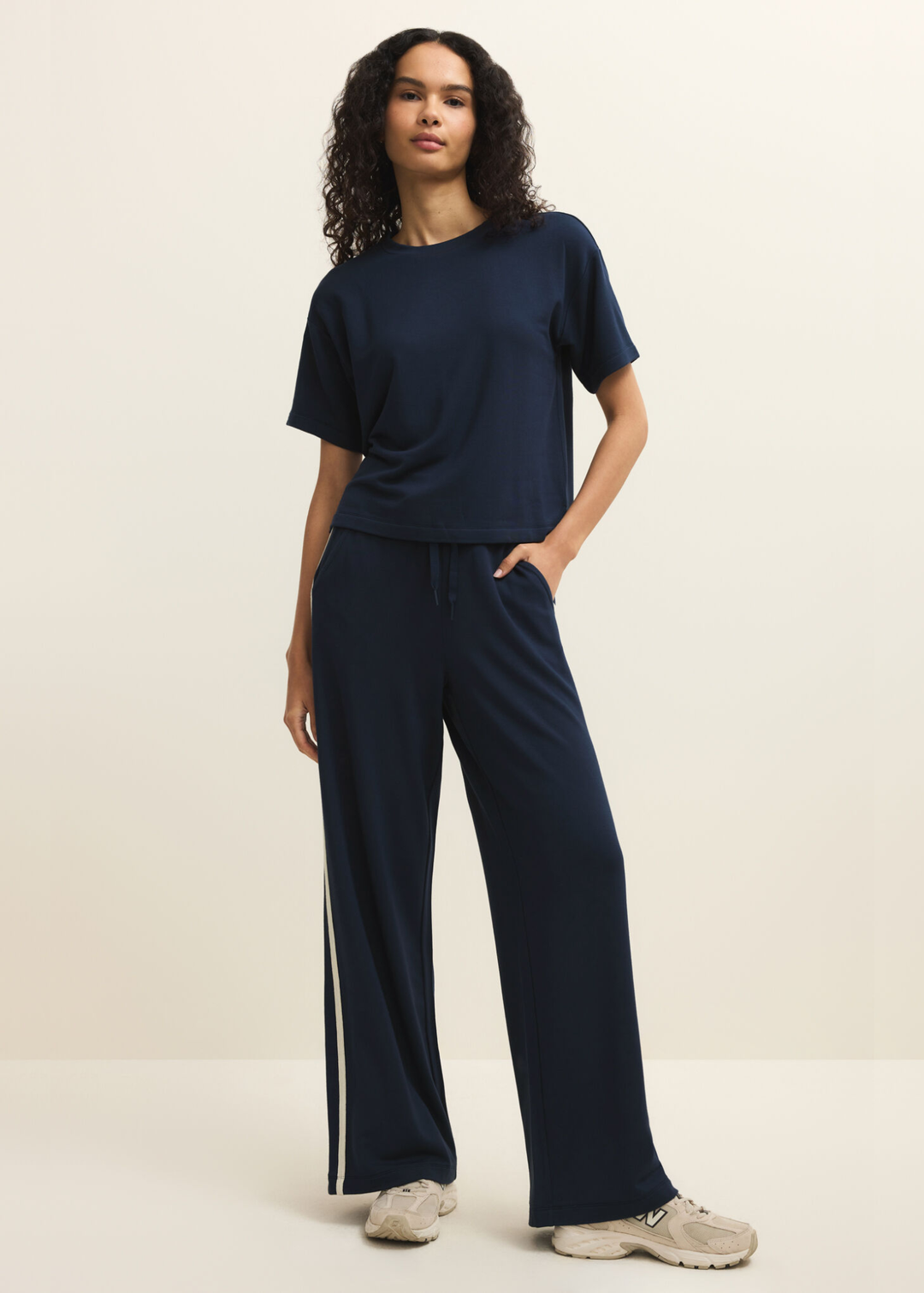 Woman wearing navy sweatpants with white side stripes and a navy tee against a white background