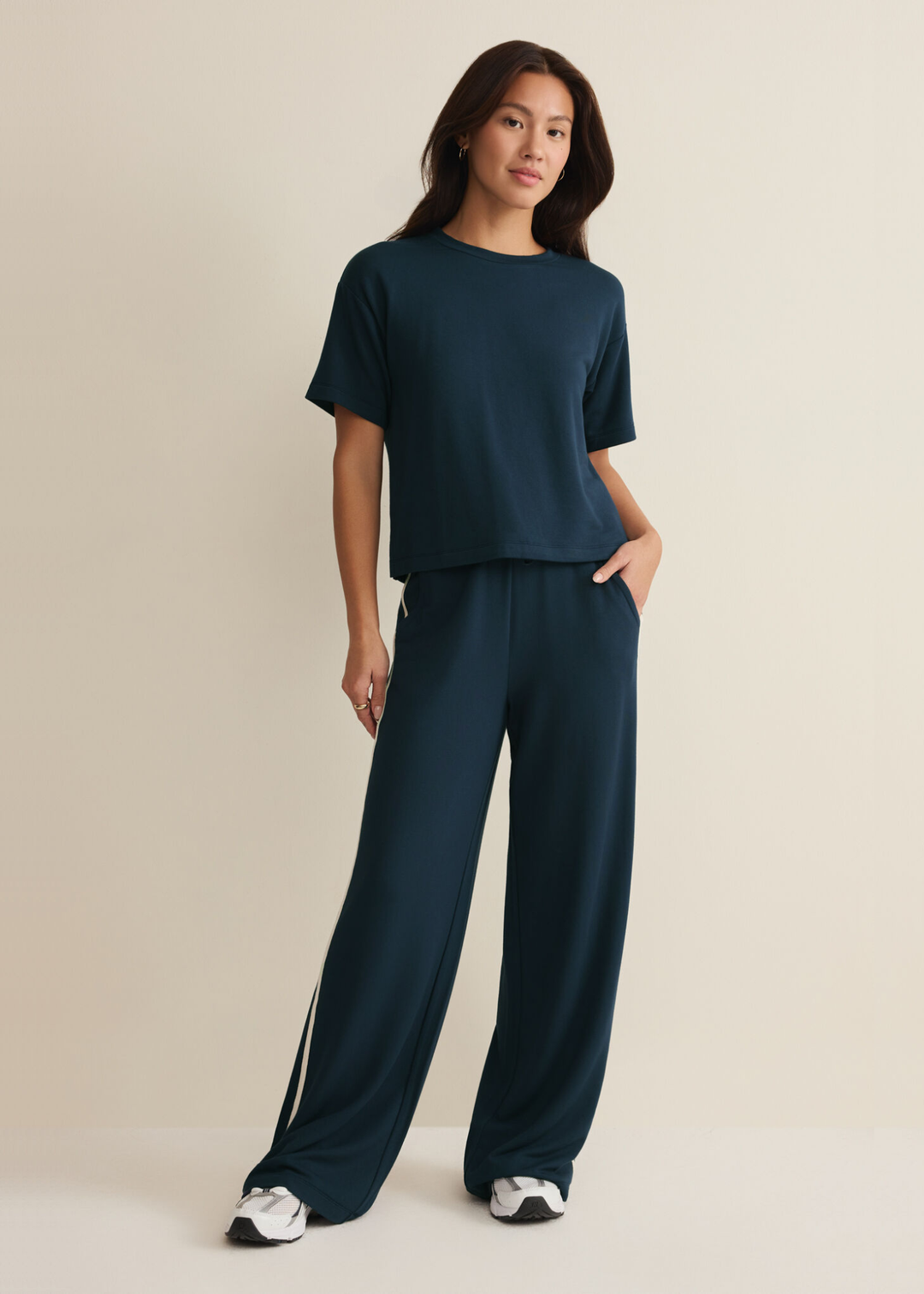 Woman wearing navy sweatpants with white side stripes and a navy tee against a white background