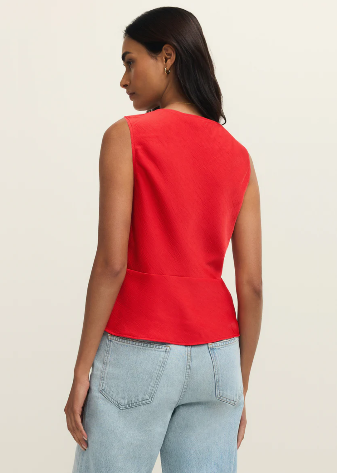 Woman turned around wearing a red satin tank top with jeans against a white background