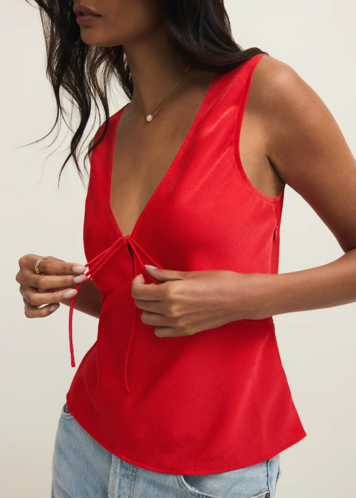 Woman wearing a red satin tank top with a front bow tie and jeans against a white background