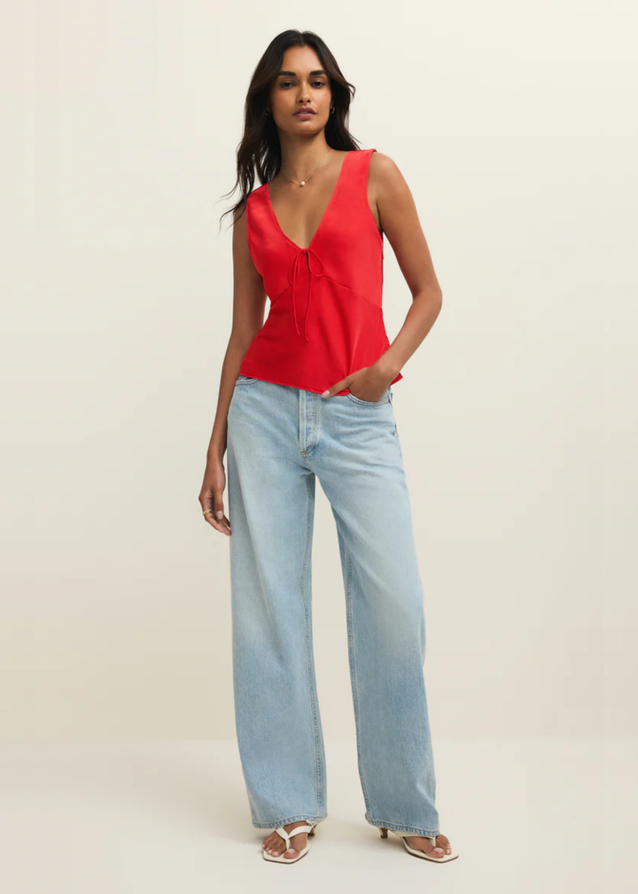 Woman wearing a red satin tank top with a front bow tie and jeans against a white background