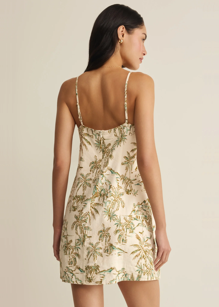 Woman turned around wearing a cream mini dress with a tropical print